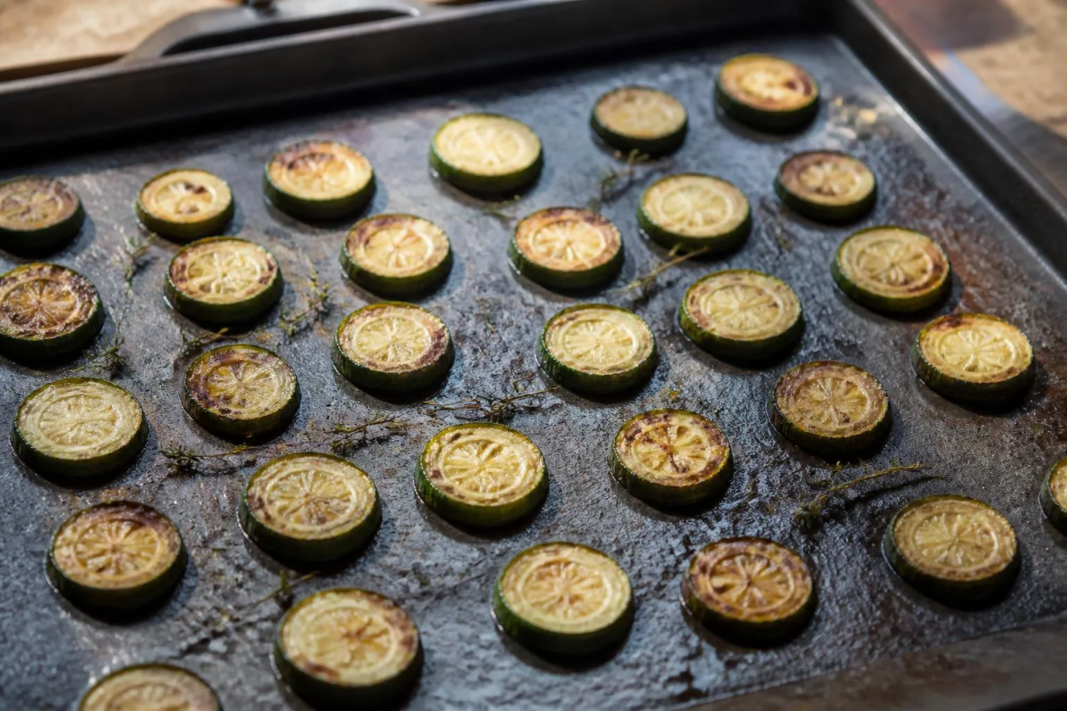 Rondelles de courgette dorées espacées sur une plaque de four en métal noirci, brins de thym