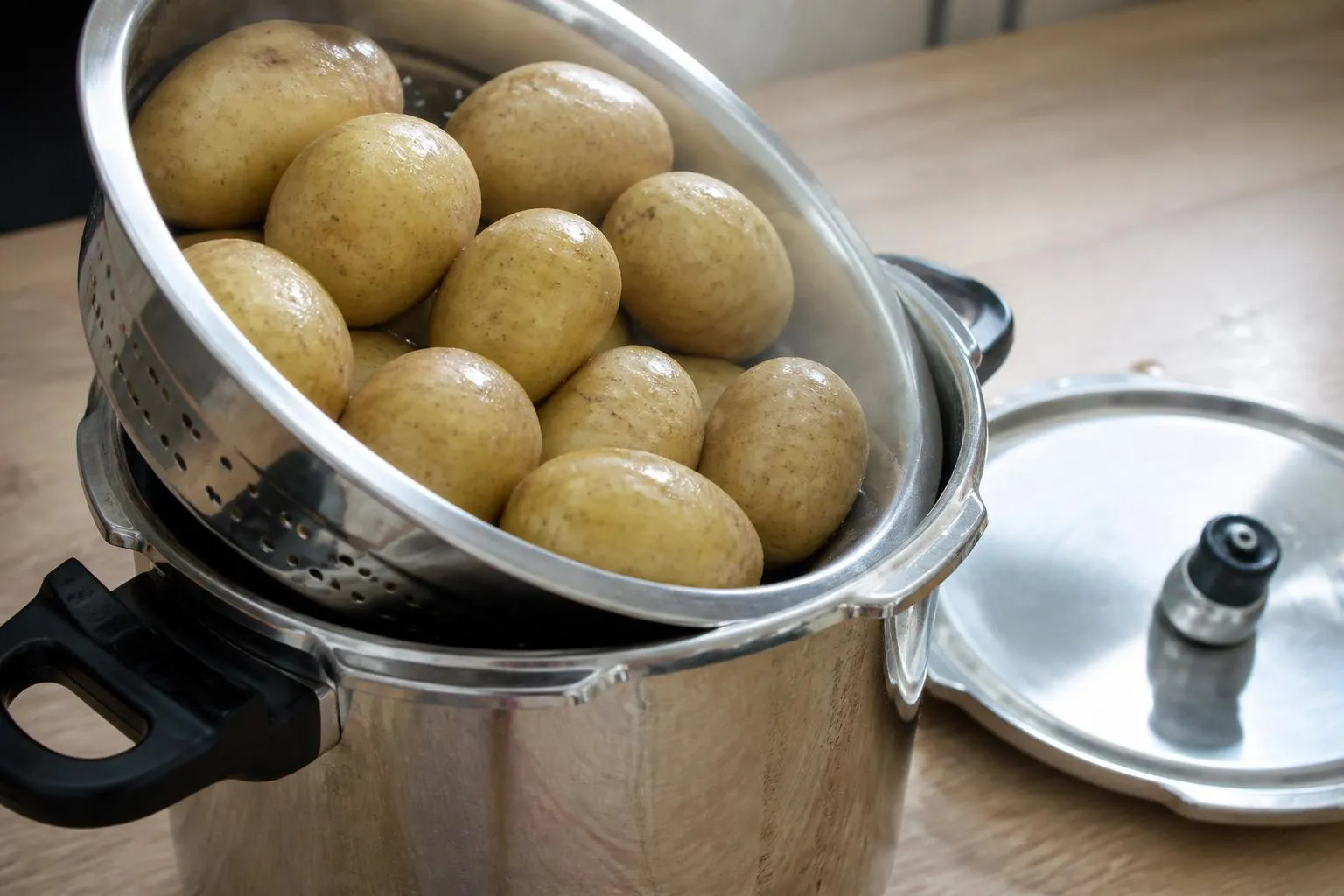 Pommes de terre entières dans un panier vapeur en inox posé sur le rebord d'une cocotte-minute ouverte